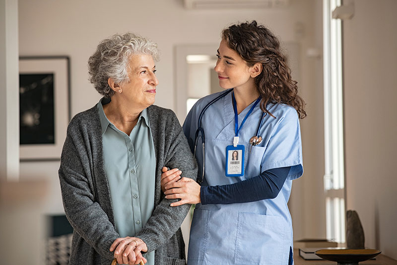 Nurse helping older woman walk down the hall
